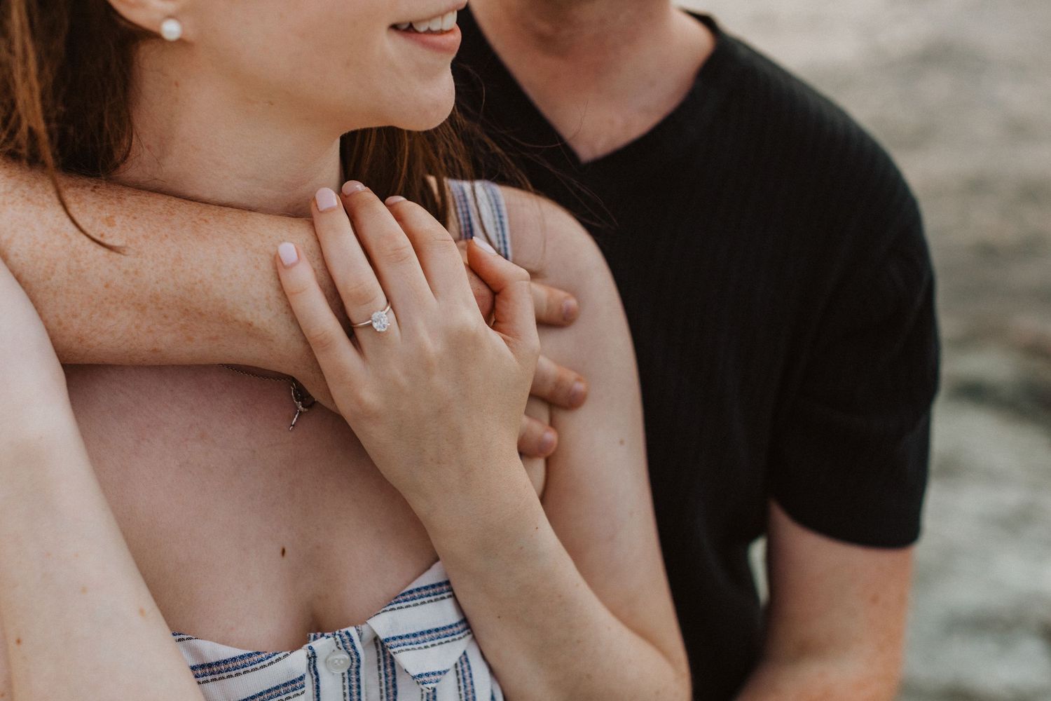 Close-up of couple embracing, woman showing off diamond engagement ring on her hand.