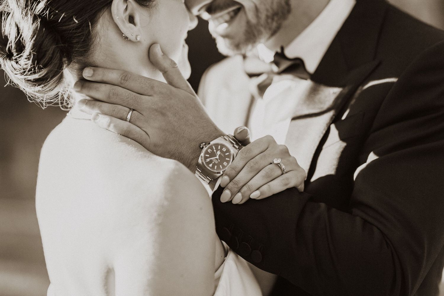 Sepia toned photo of groom tenderly holding brides neck wearing a classic watch at wedding.
