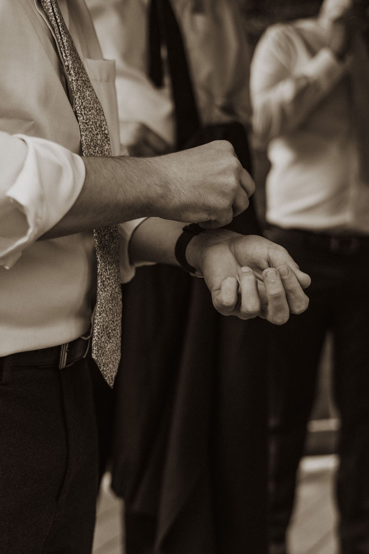 Groom adjusting his watch cufflinks in sepia tone, wearing white shirt and sparkly tie.