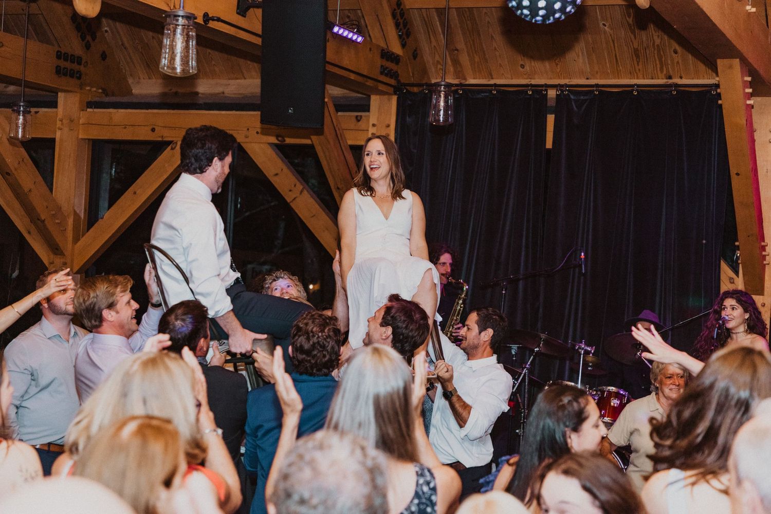 Bride and groom stand elevated above cheering wedding guests on a dance floor inside a rustic barn venue.