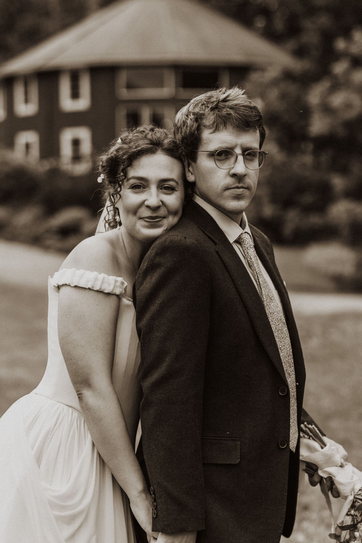 Bride and groom pose back-to-back in sepia-toned outdoor wedding portrait.