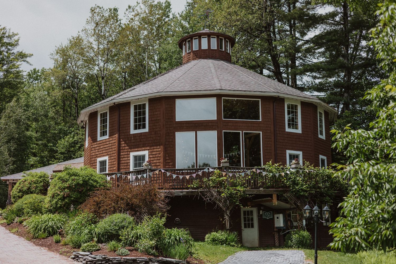 Unique octagonal brick house with a cupola roof surrounded by lush green trees and landscaped gardens.