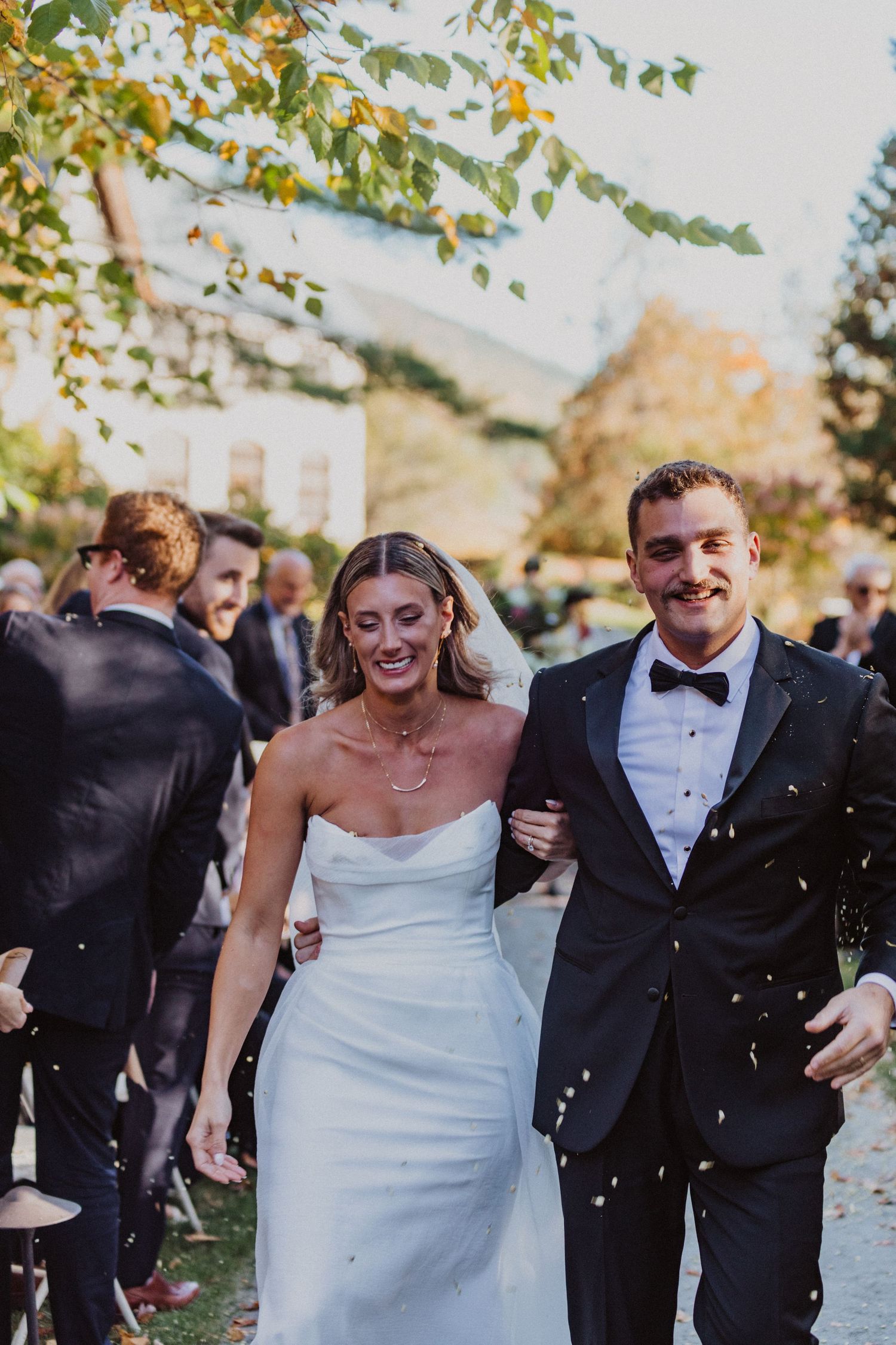 Happy bride and groom walk through confetti shower at their outdoor autumn wedding celebration.
