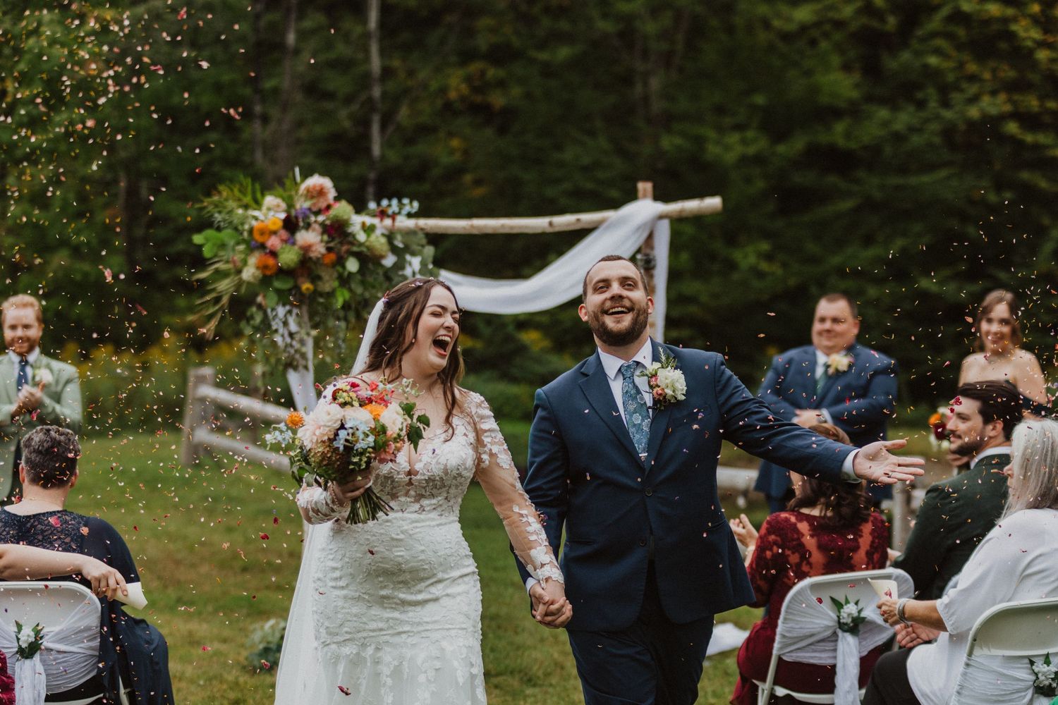 Joyful bride and groom walking back down the aisle after outdoor wedding ceremony with confetti.