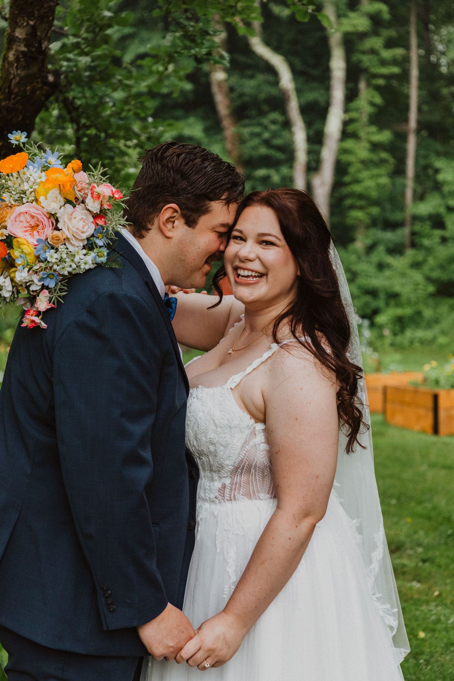 Joyful bride in white gown laughing with groom in navy suit during outdoor wedding ceremony.