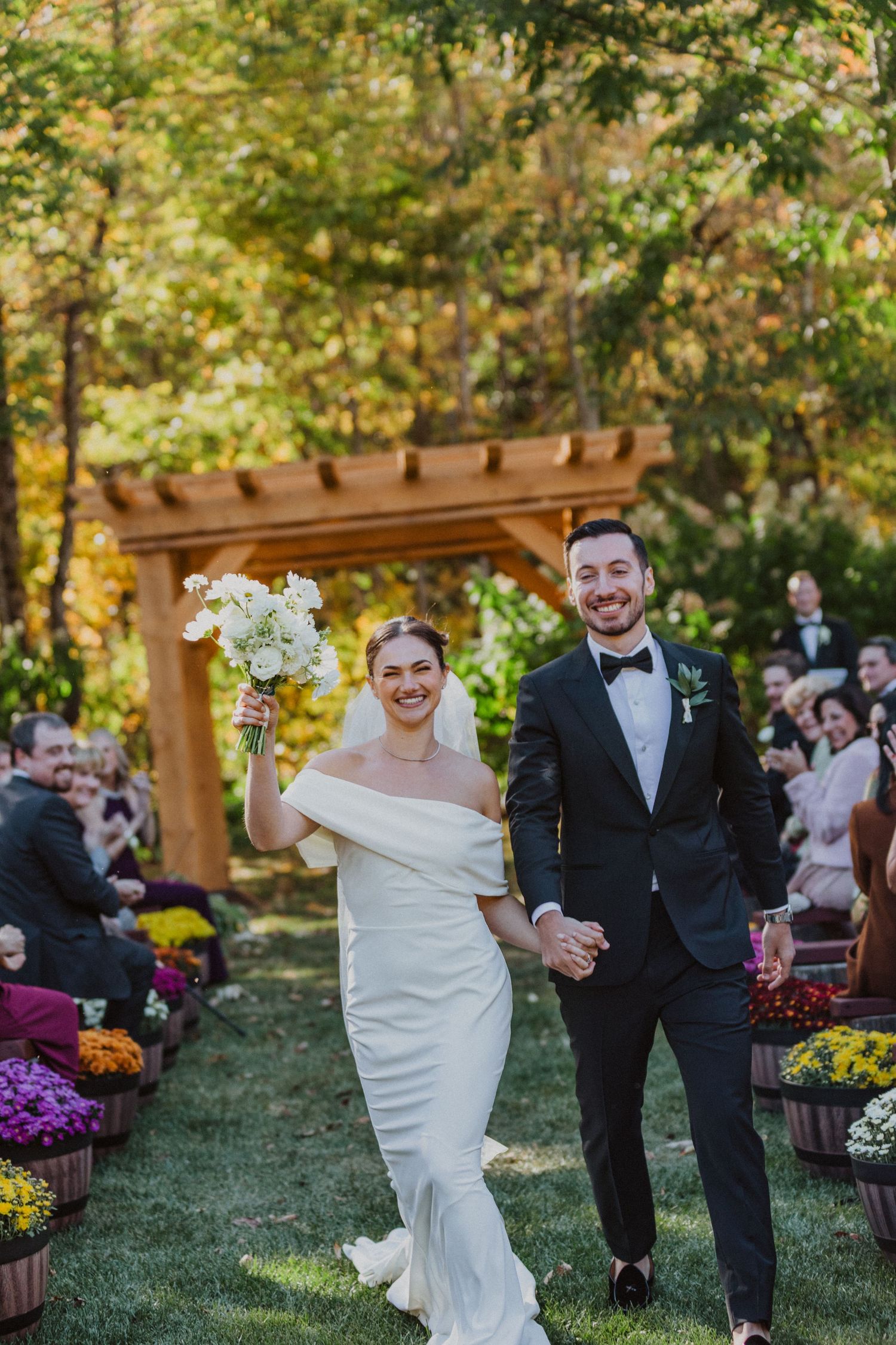 Joyful bride and groom walk down the aisle at an outdoor fall wedding ceremony surrounded by guests.