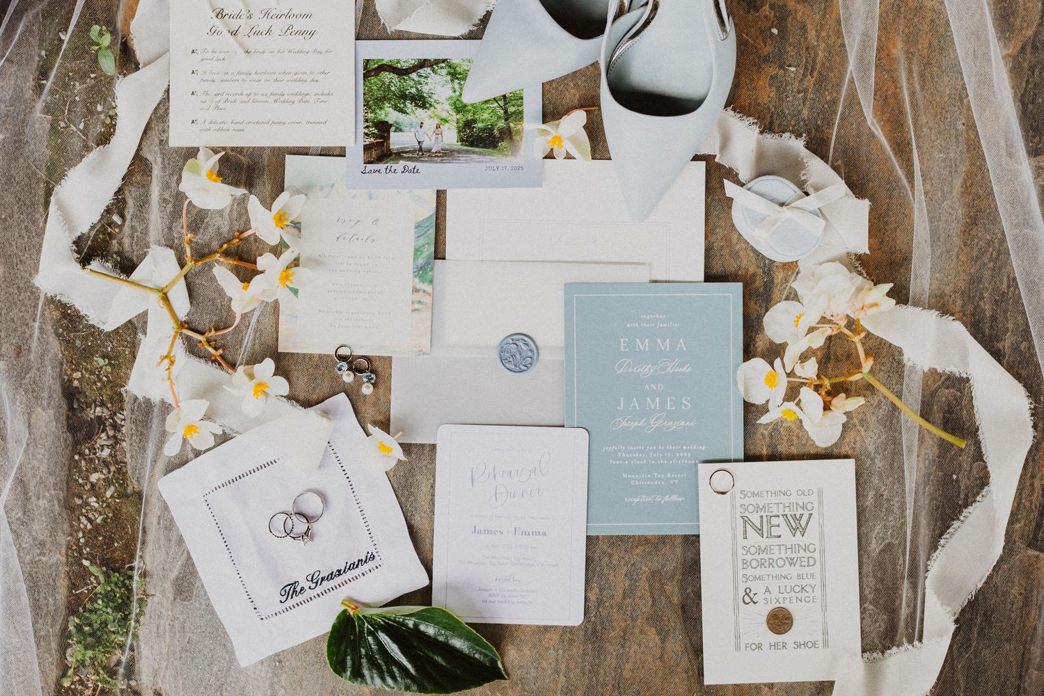 Elegant wedding invitation suite with dusty blue accents, wax seal, and floral details on wood table.