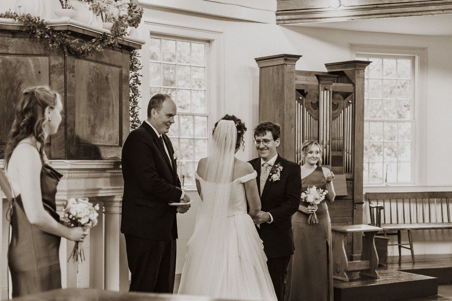 Black and white wedding ceremony photo of bride and groom exchanging vows at altar in elegant church.