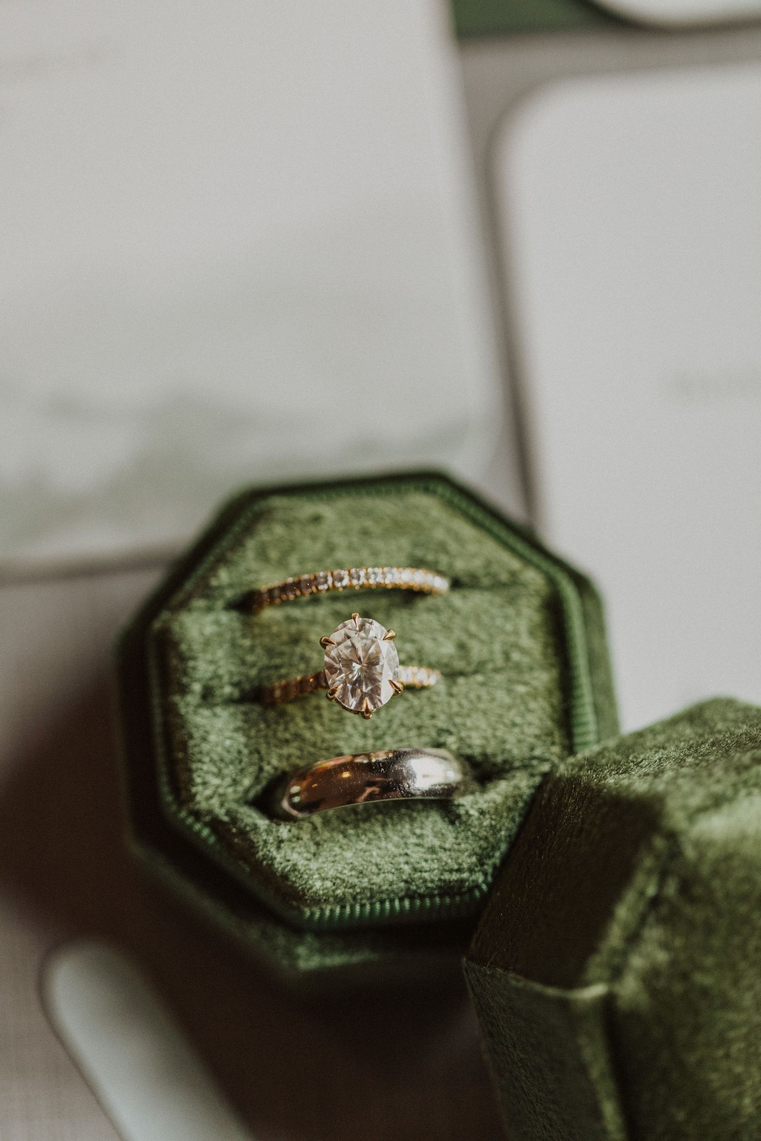 Three wedding rings displayed in a green velvet octagonal ring box, including a diamond solitaire engagement ring.