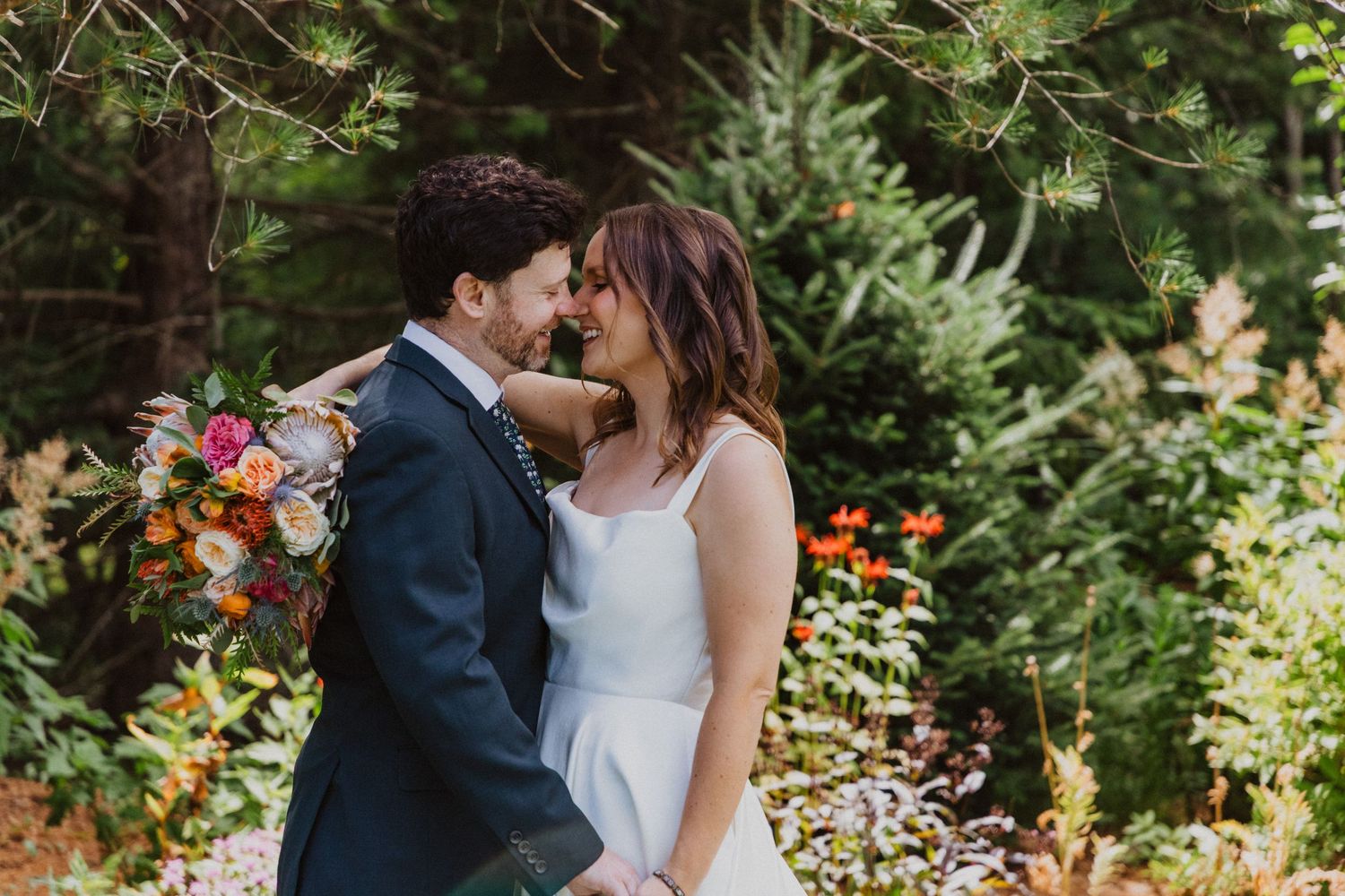 A couple shares a romantic moment surrounded by lush greenery and colorful flowers at their wedding.