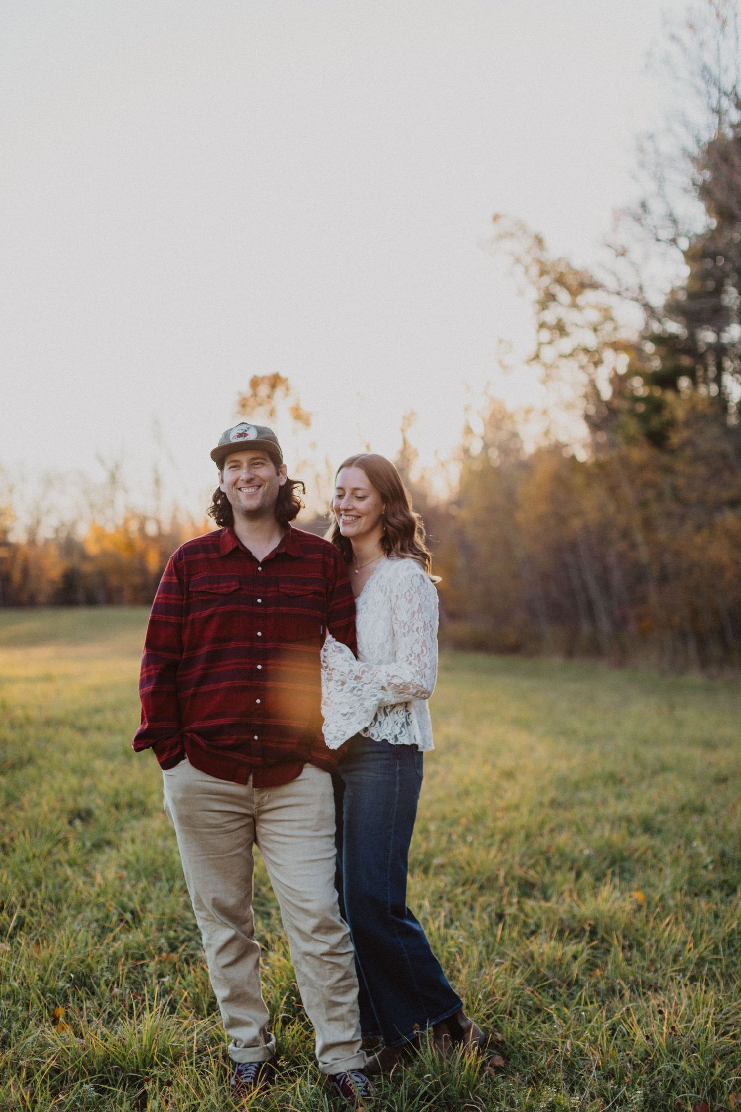 Couple smiling together in a sunlit autumn field during golden hour engagement photo session.