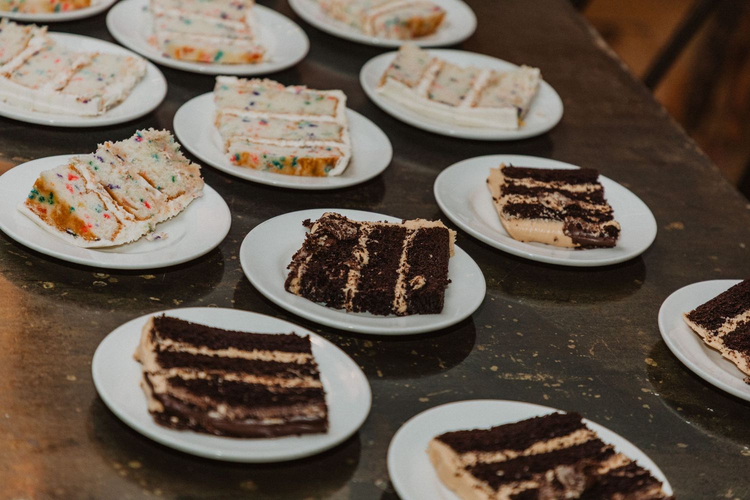 Assorted wedding cake slices including chocolate and confetti varieties plated on white dishes.