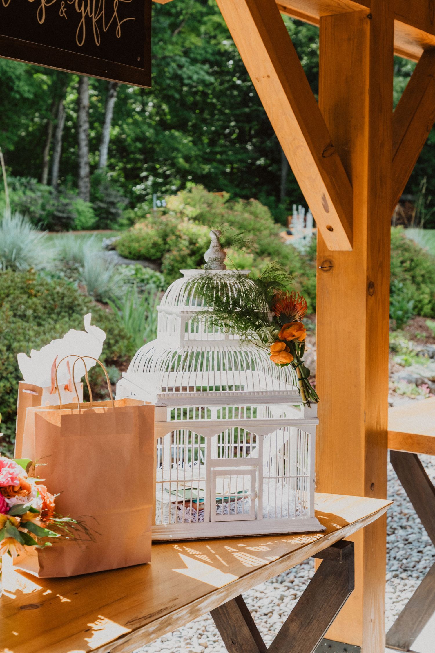 Decorative white birdcage centerpiece with flowers on a wooden table at an outdoor rustic wedding venue.