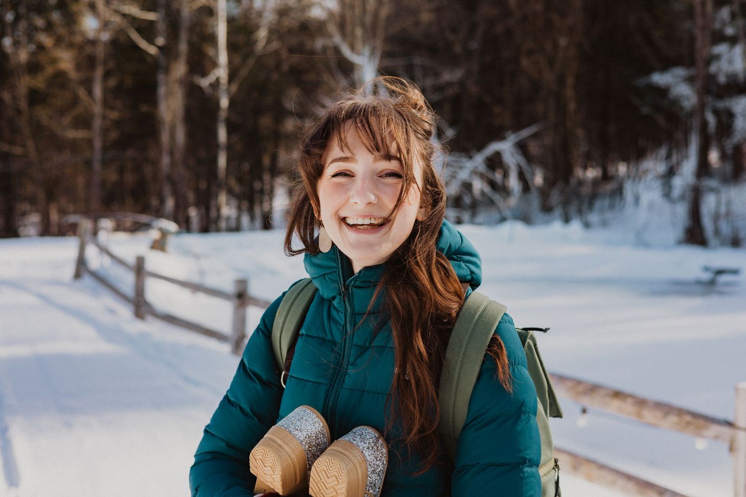 Happy young woman with red hair smiles outdoors in snowy winter forest landscape.