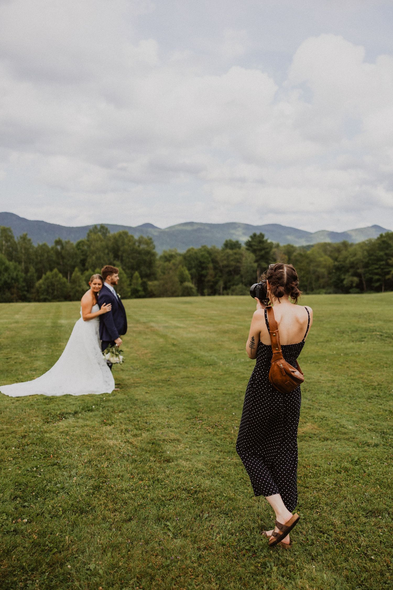 Wedding photographer captures bride and groom embracing in lush green mountain meadow.