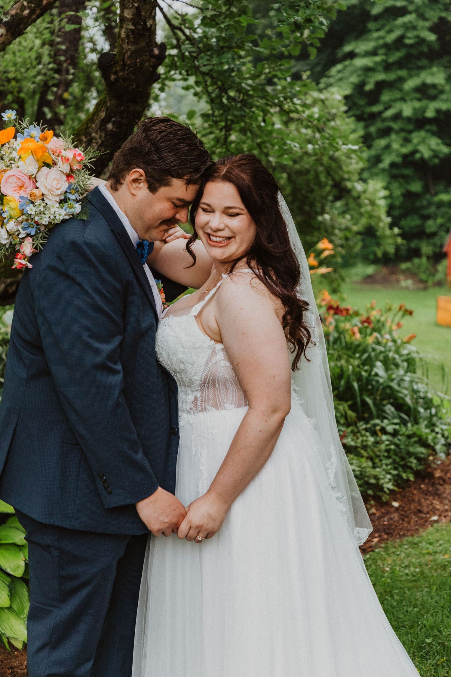 Bride and groom share a tender moment outdoors, with the groom kissing her cheek as she smiles joyfully.