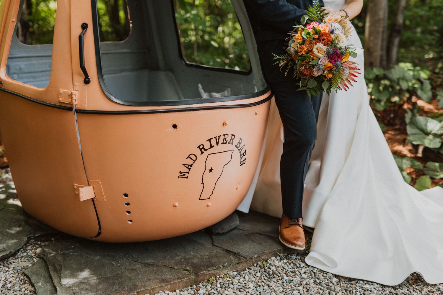 Bride and groom posing beside a vintage Mad River Glen ski gondola, bride holding a colorful wildflower bouquet.