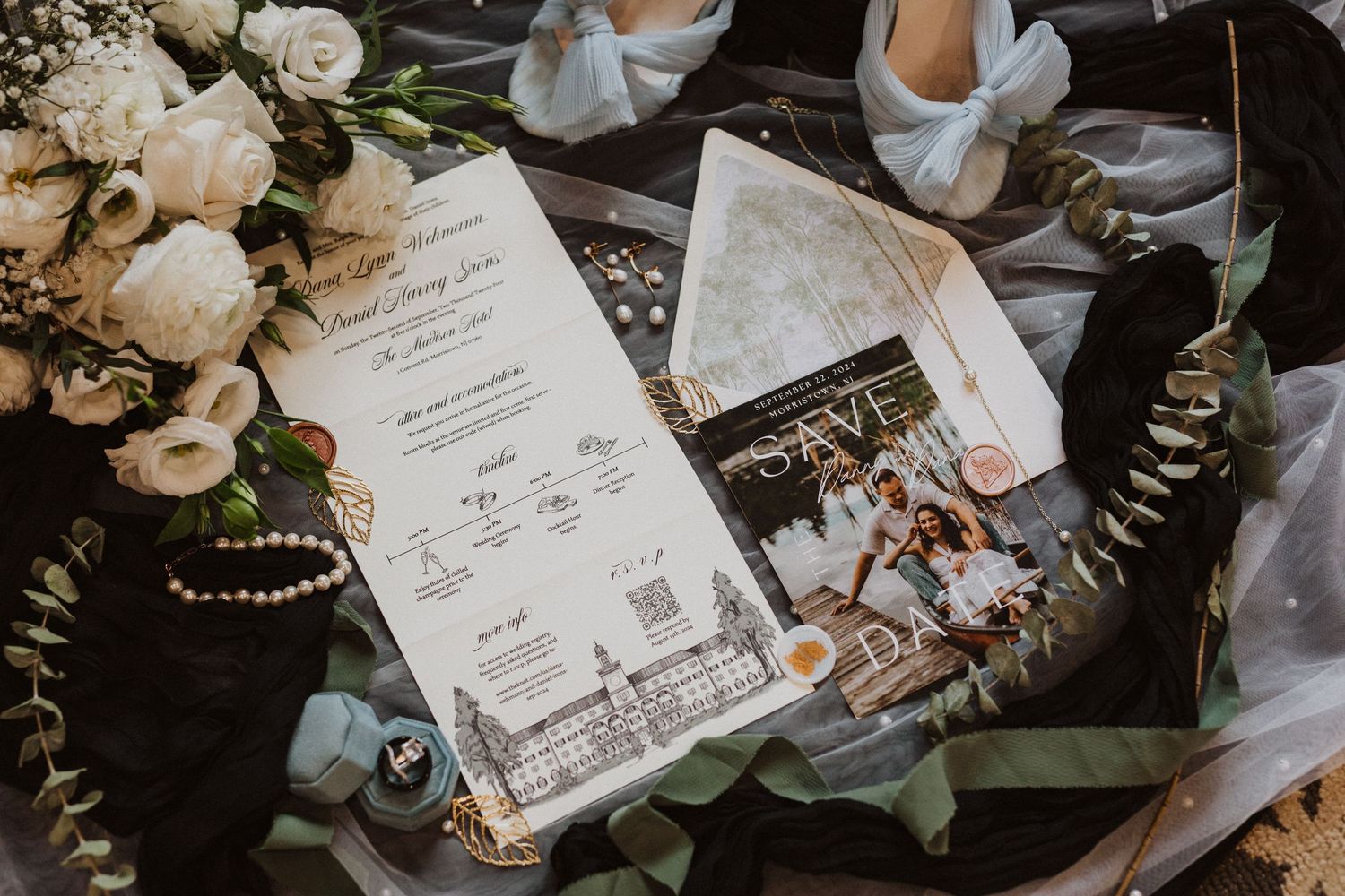 Detailed wedding invitation suite with illustrated venue, QR code, and couple photo on dark surface.