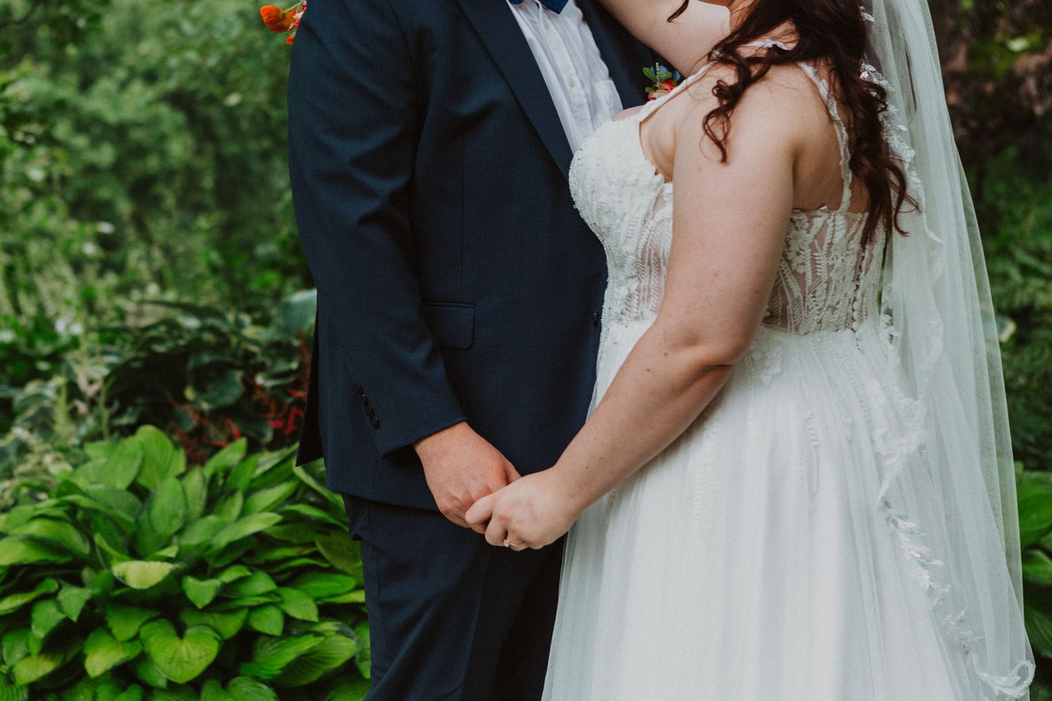 Bride and groom holding hands in a lush garden setting on their wedding day.