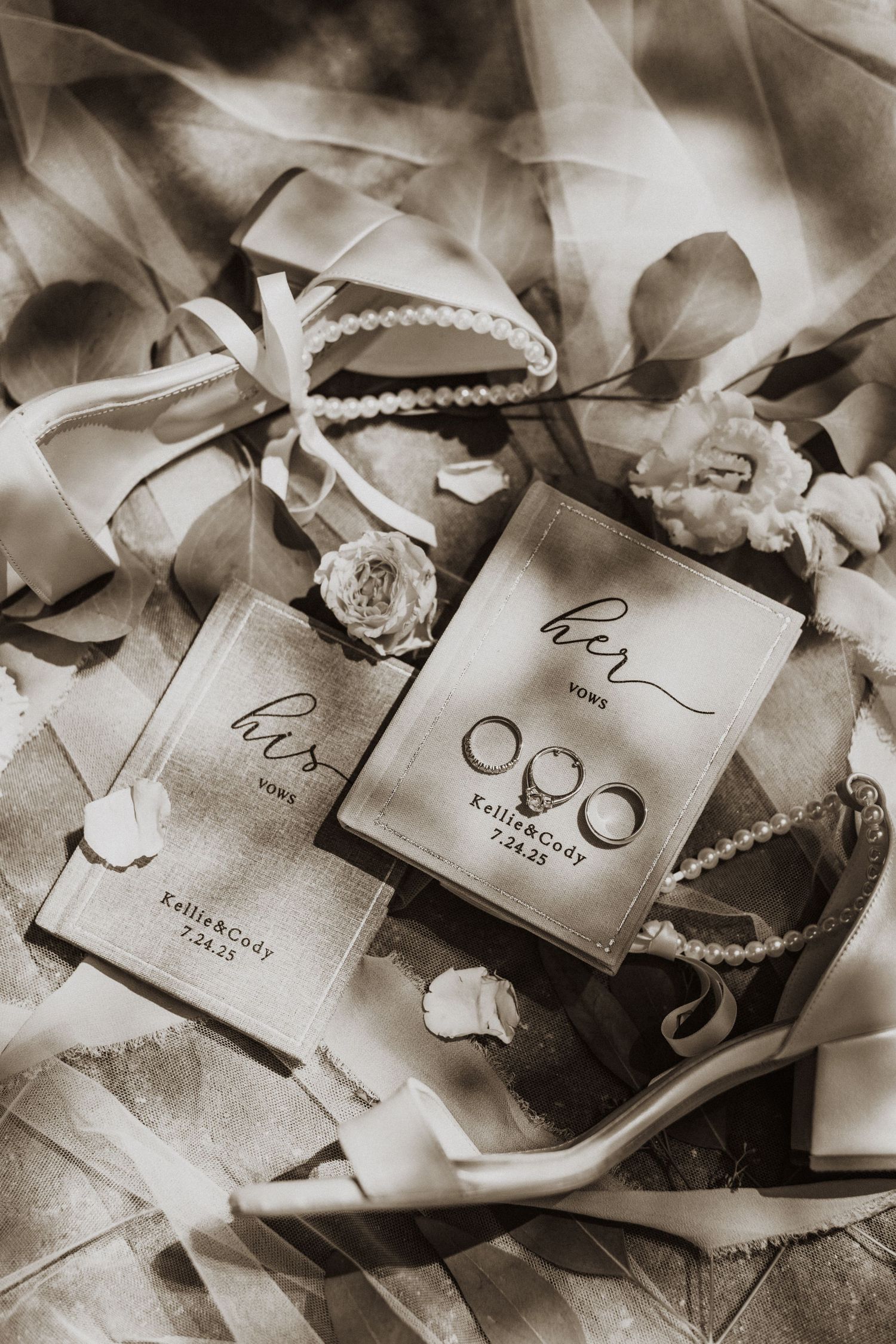 Wedding vow books and rings styled with pearls and flowers in sepia tone flatlay.