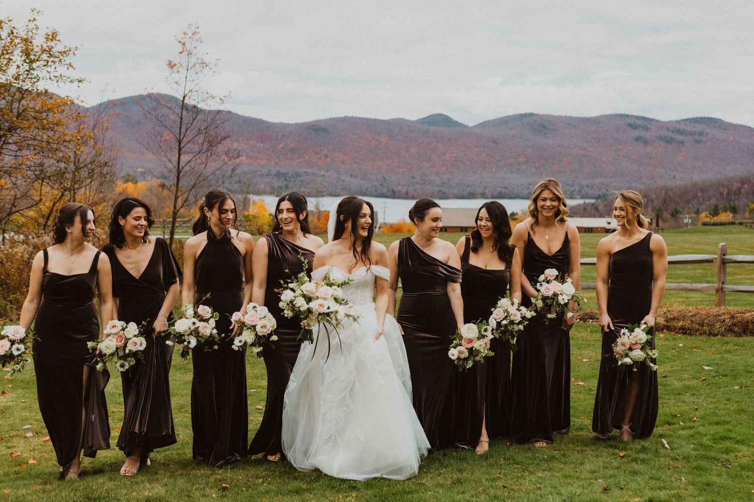 Bride with bridesmaids in dark dresses holding white bouquets with stunning autumn mountain backdrop.