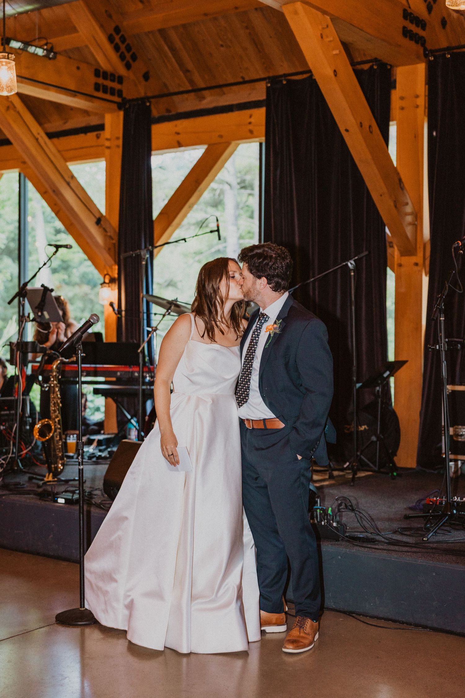 Bride and groom share their first kiss inside a stunning timber-frame wedding reception venue with a live band.