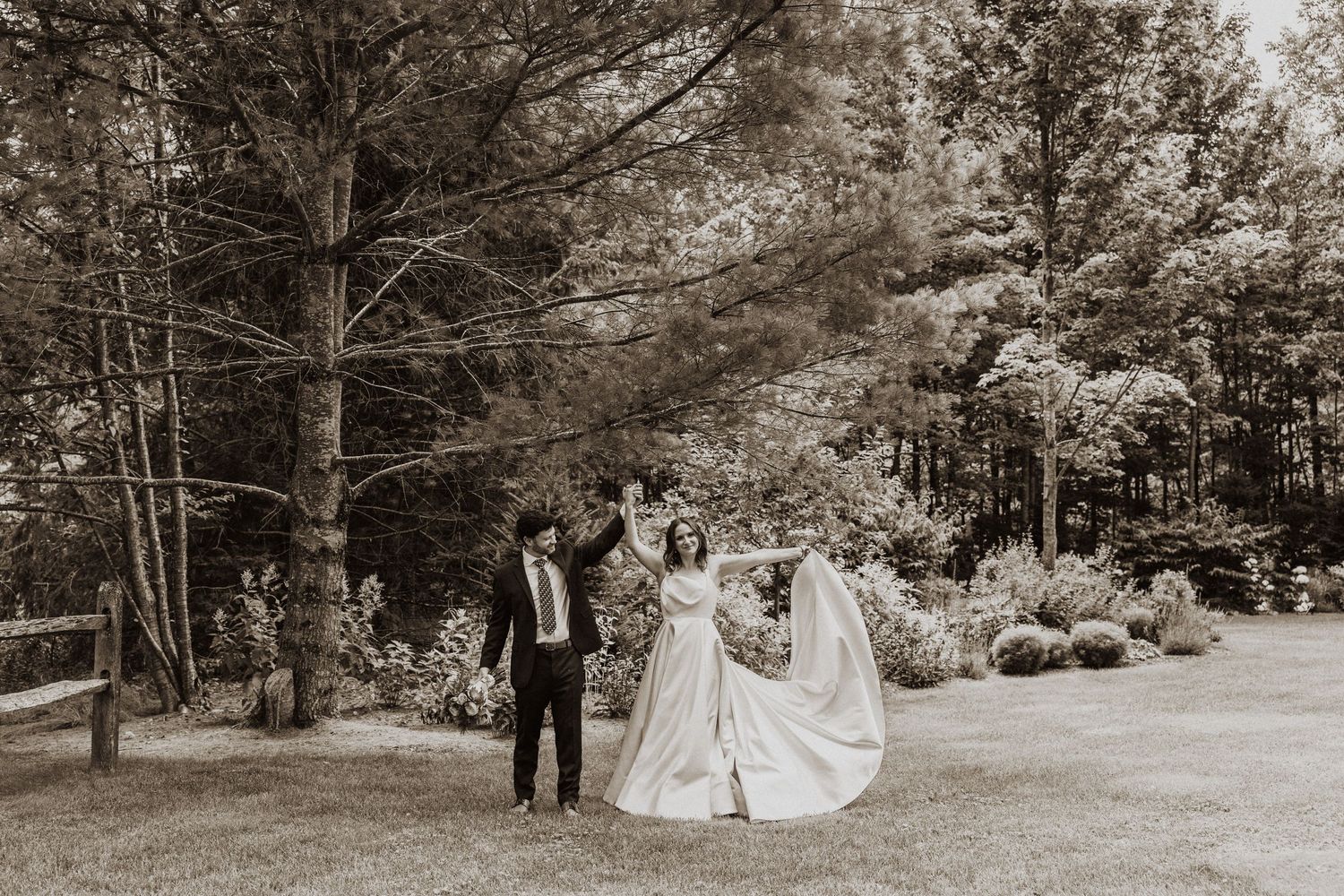 Black and white photo of bride and groom dancing outdoors in lush garden setting on their wedding day.