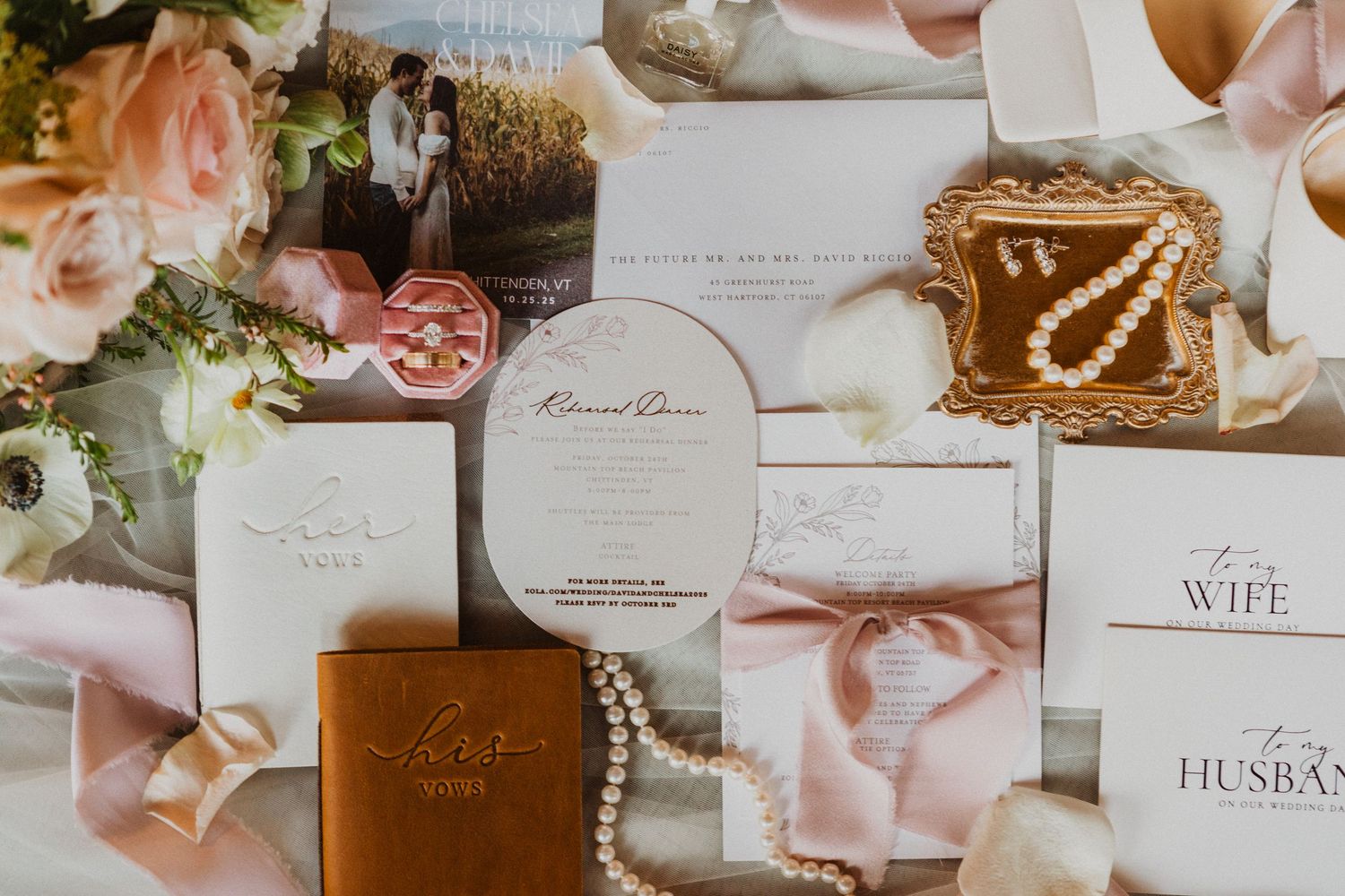 Elegant wedding stationery flat lay with floral arrangements, pearl jewelry, and blush pink ribbons.