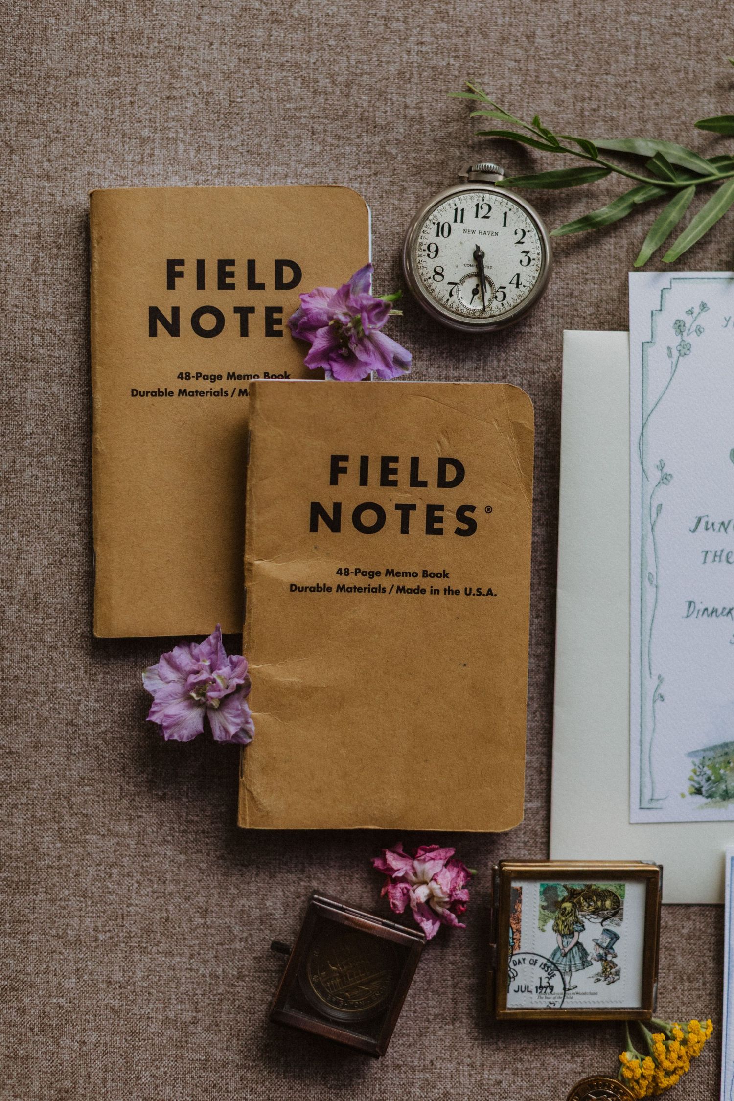 Field Notes notebooks flat lay with vintage pocket watch, purple flowers, and wedding stationery.