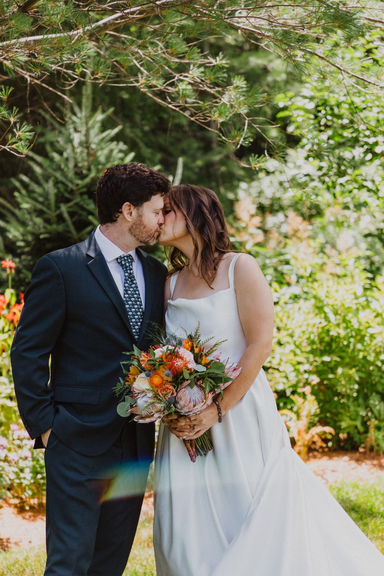 Bride and groom sharing a kiss in lush garden setting, bride holding colorful bridal bouquet.