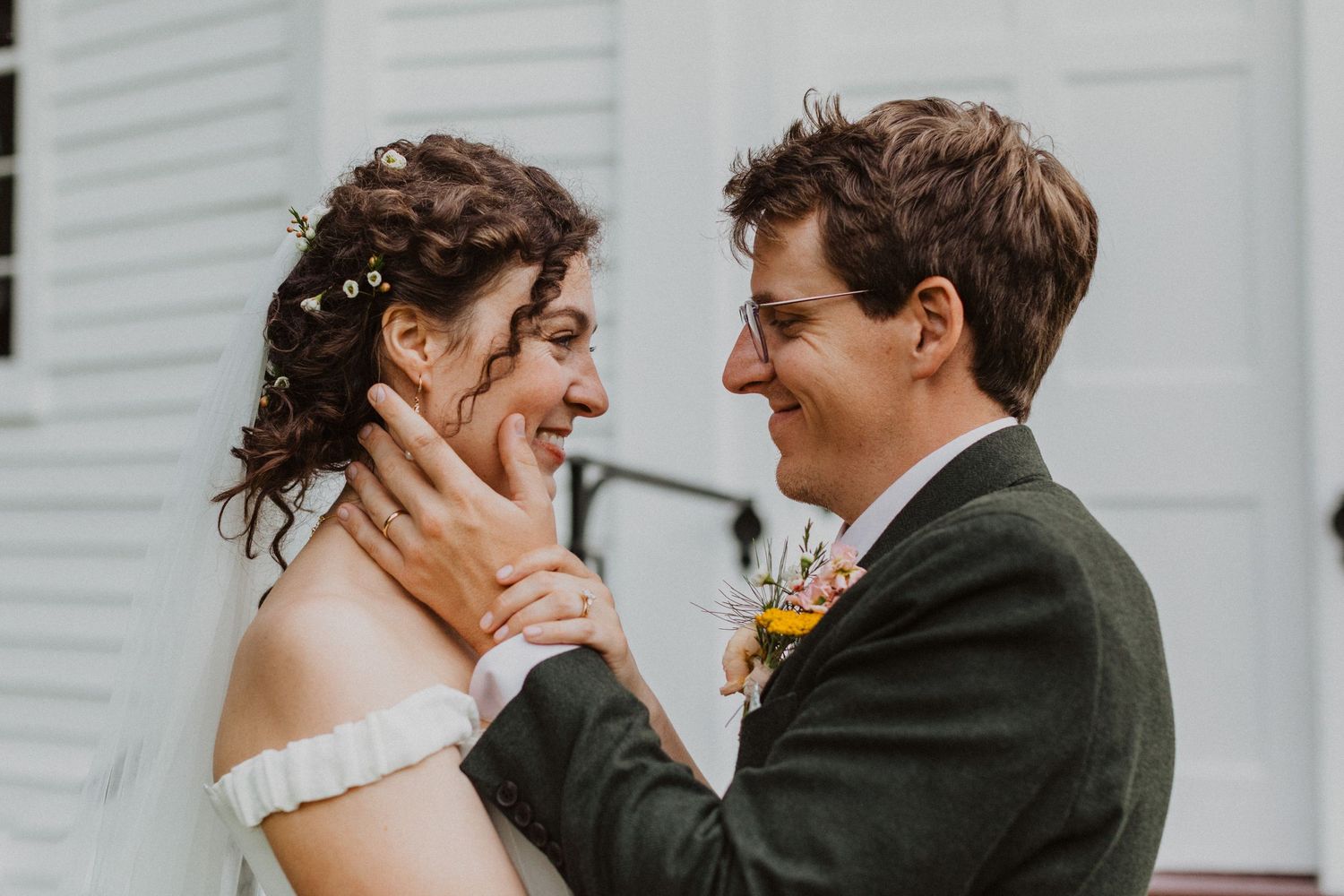Joyful bride and groom gazing at each other, groom cupping bride's face outside white chapel.