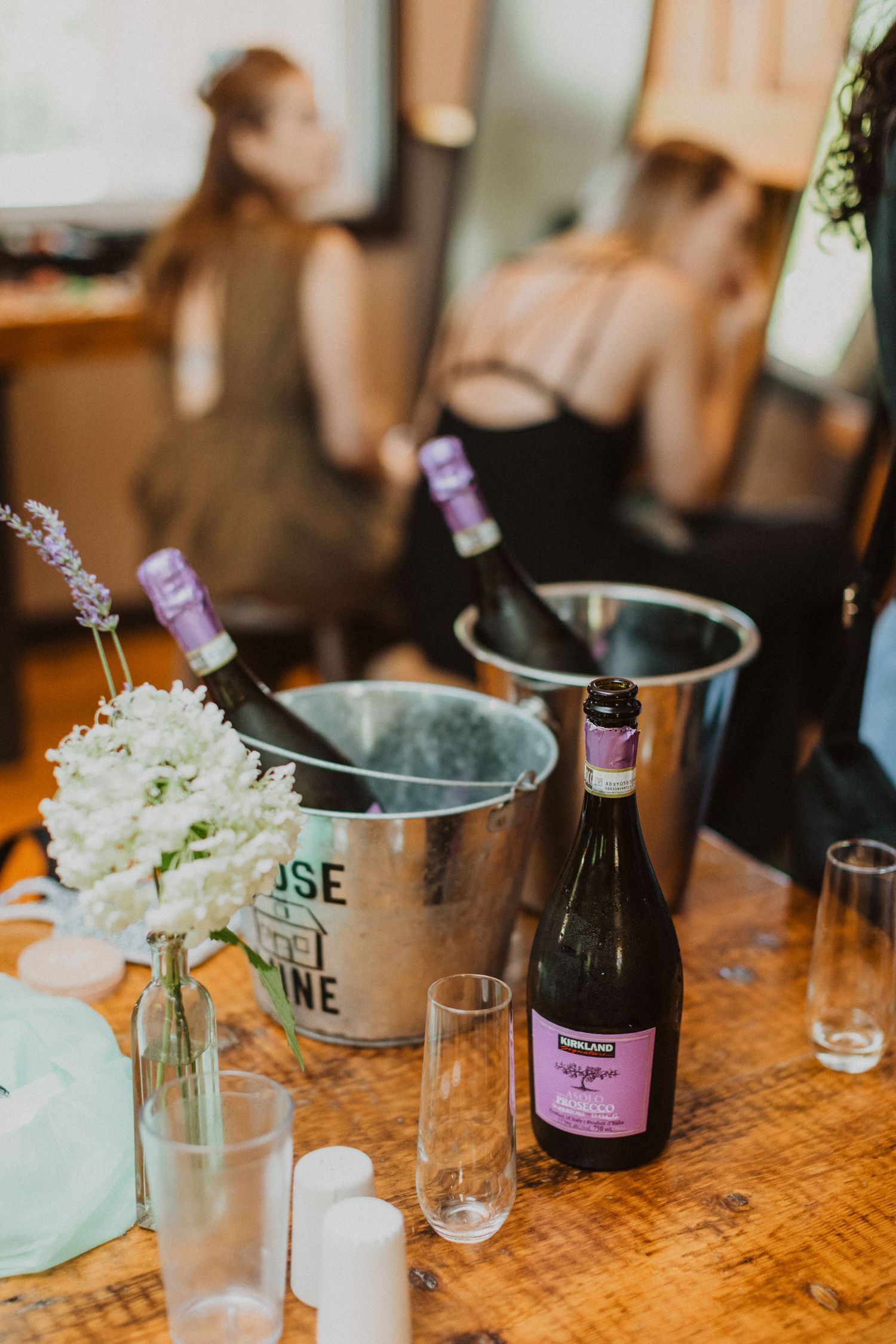 Champagne bottles chilling in ice buckets with white flowers and glasses on a wooden table at a wedding reception.