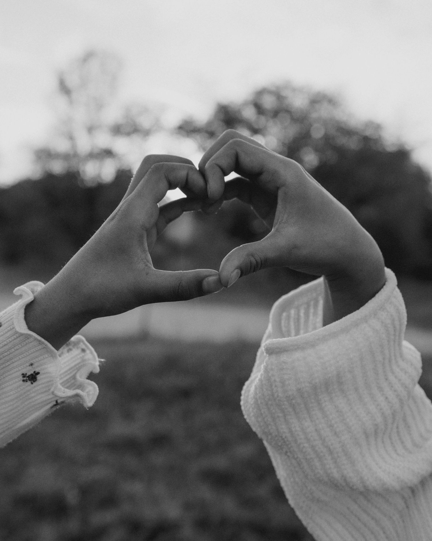 Two hands forming a heart shape together in black and white outdoor photo.