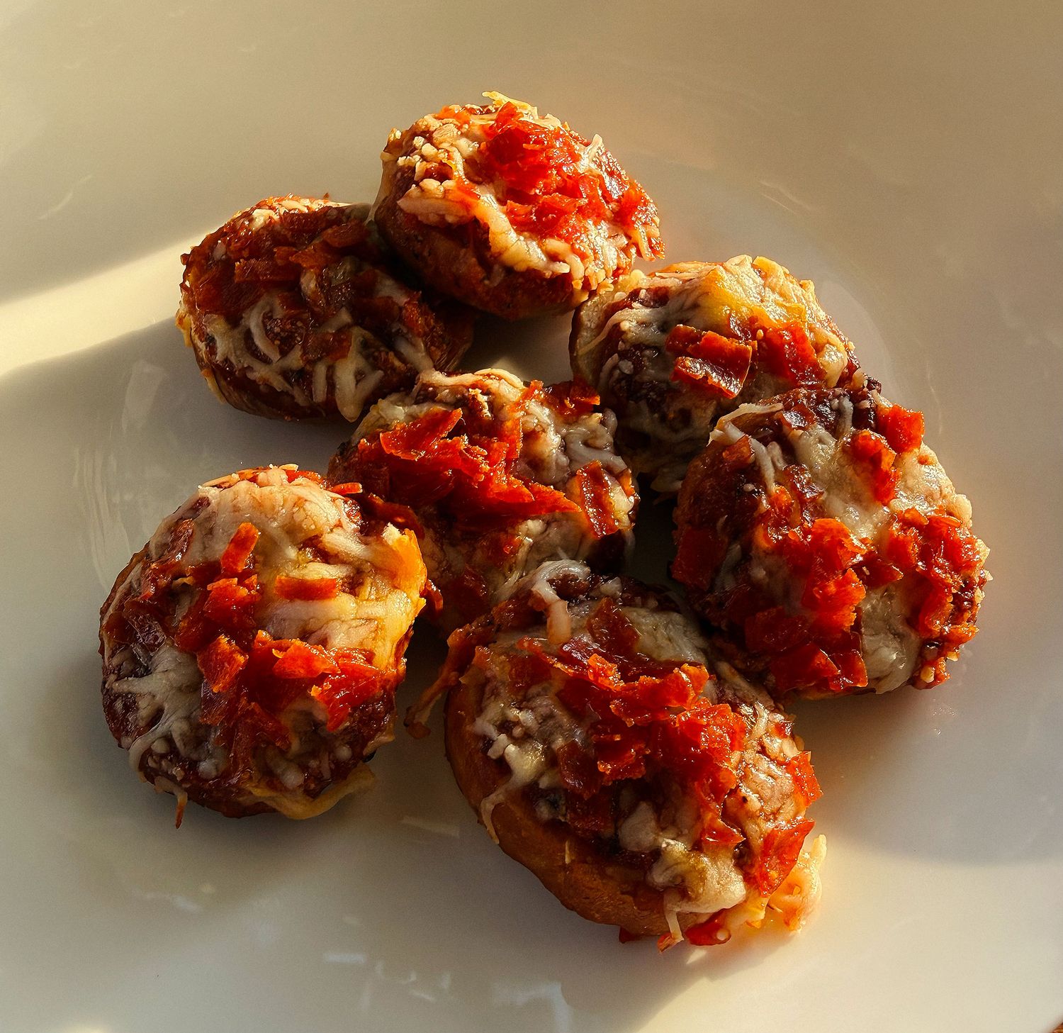 Mini pizza bagel bites topped with tomato sauce, melted cheese, and meat on a white plate.