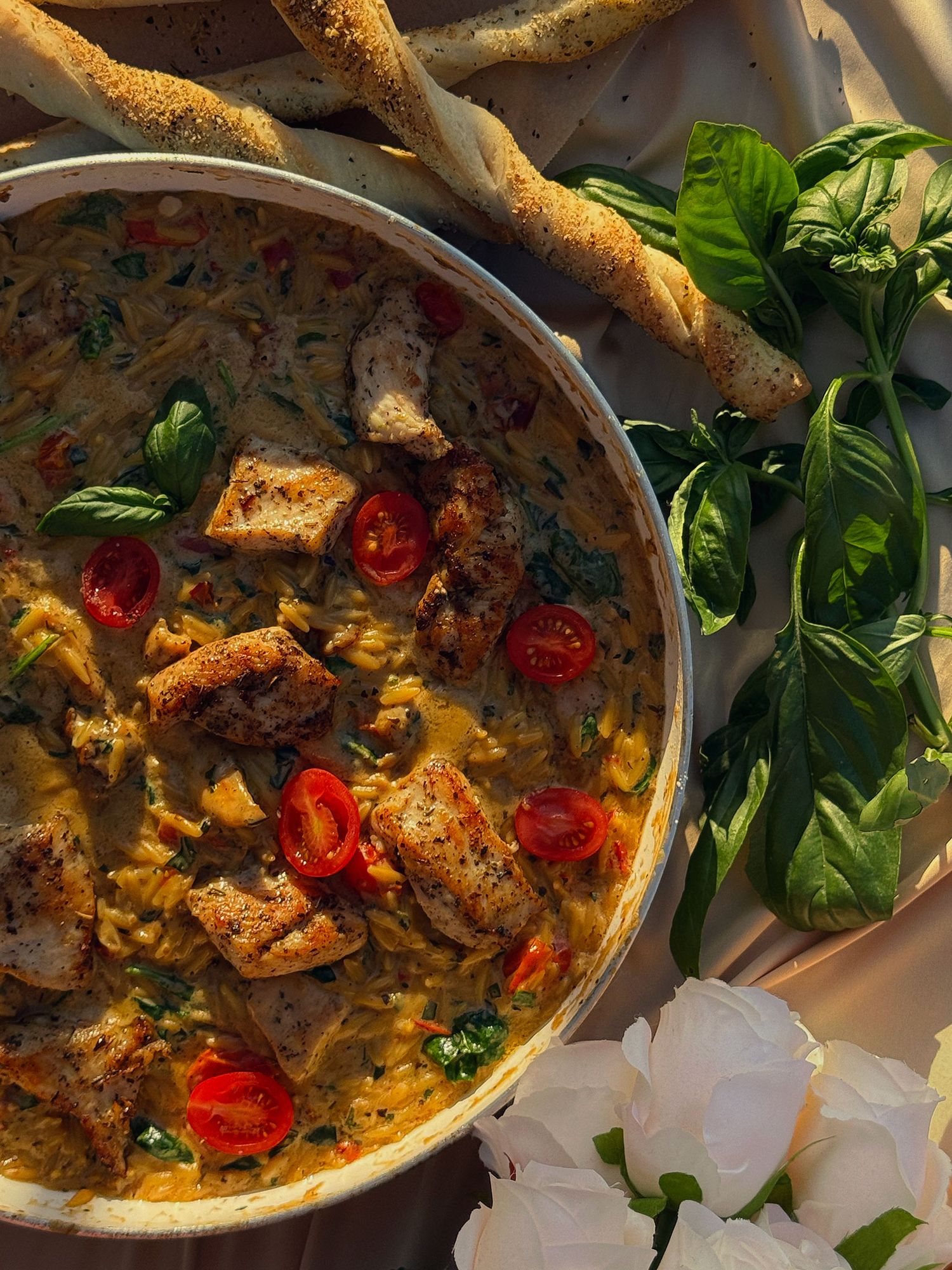 Creamy chicken and tomato stew with fresh basil, cherry tomatoes, served in a rustic pan with breadsticks.