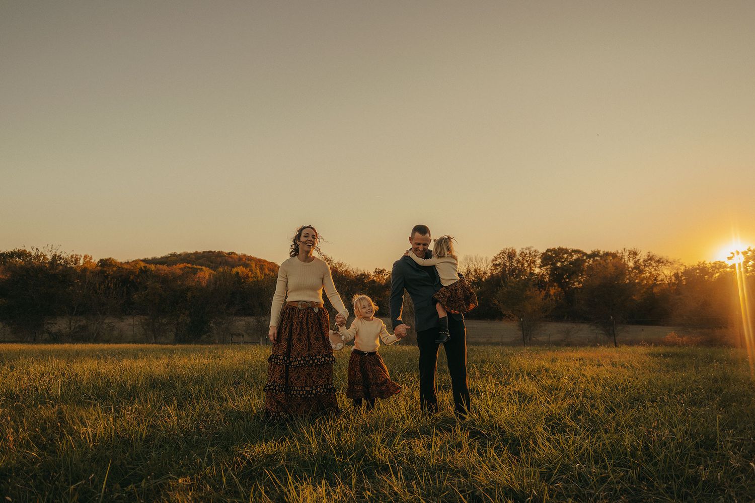 Happy family of four holding hands in green meadow during beautiful golden sunset.