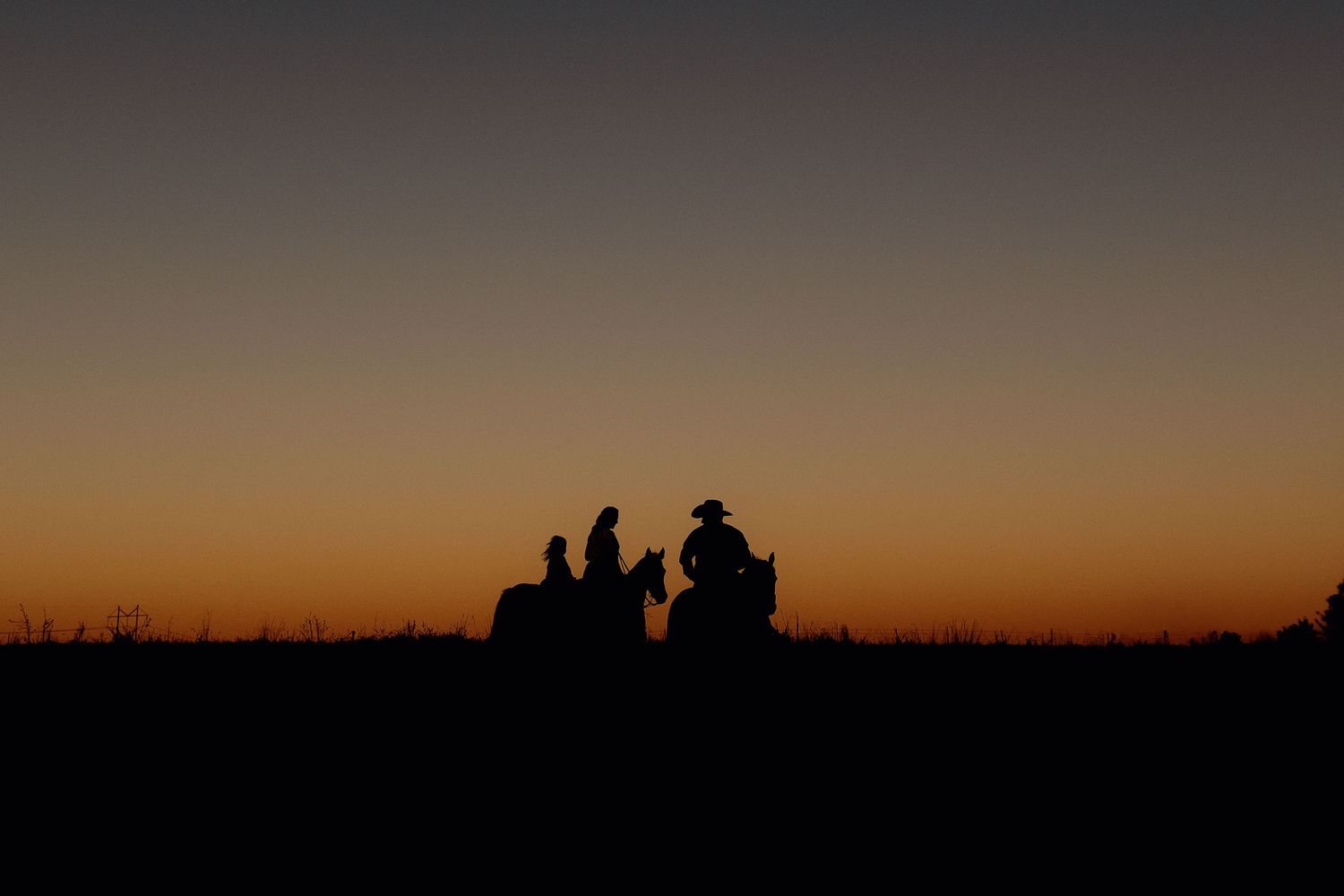 Silhouettes of cowboys on horseback against a vibrant orange and blue sunset sky on open plains.