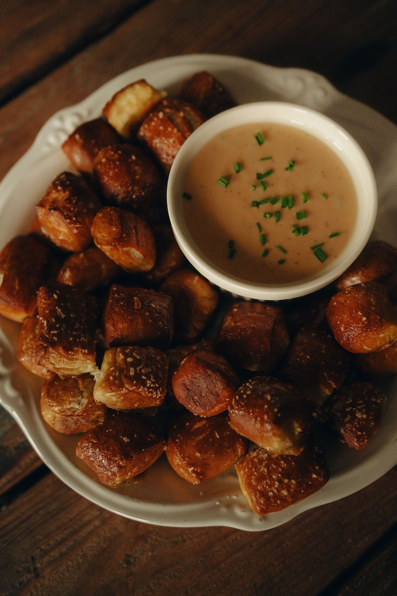 Soft pretzel bites served on a white plate with a creamy beer cheese dipping sauce garnished with chives.