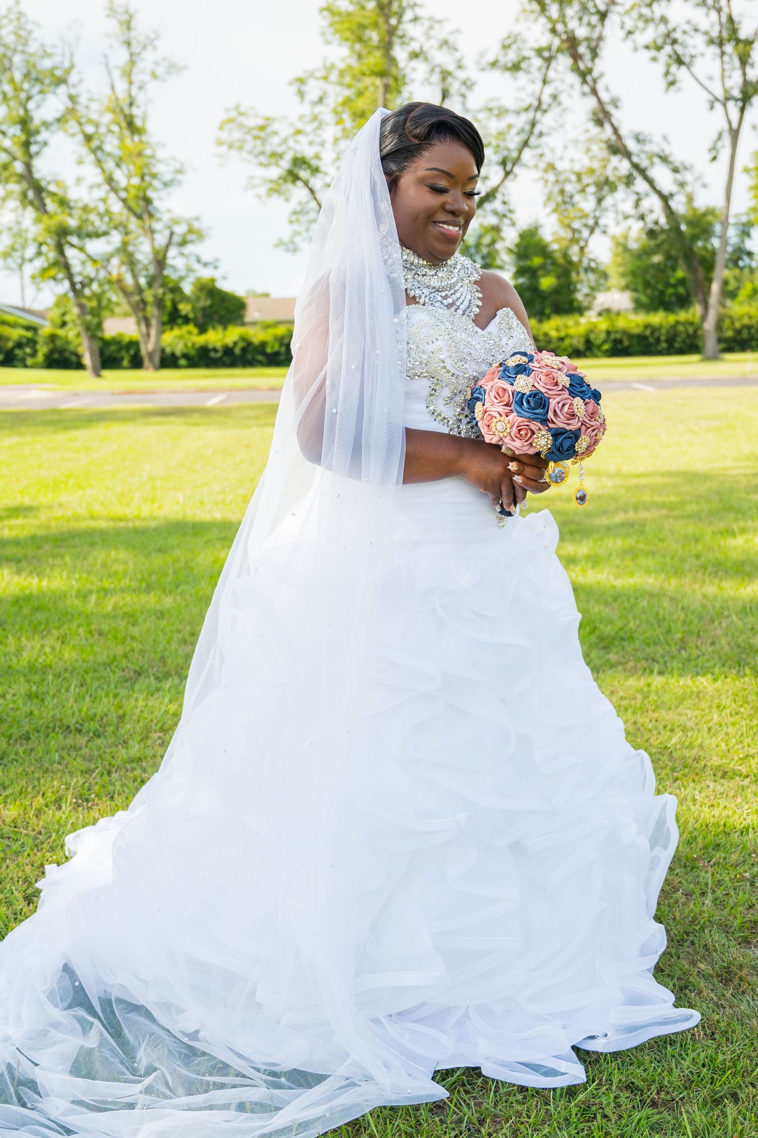 Beautiful Black bride in elegant white ball gown with veil holding pink and navy bouquet outdoors.