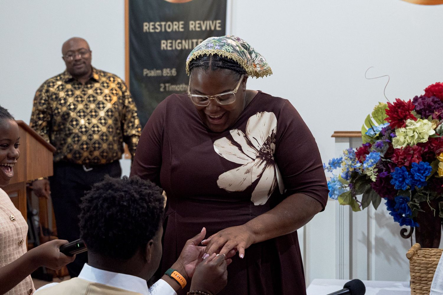 Woman in floral dress presenting ring to kneeling man inside a church during proposal.