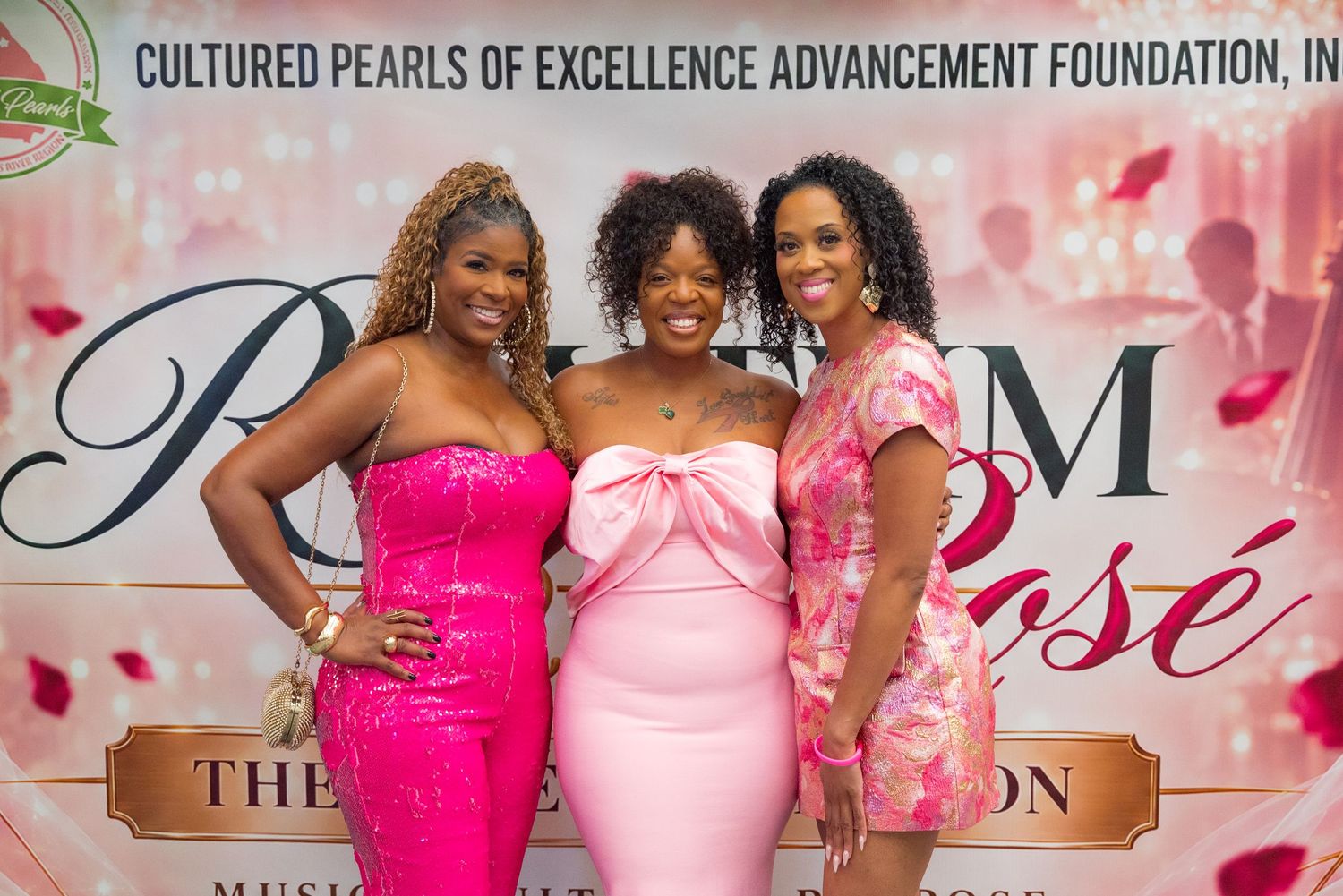 Three women in pink dresses smile together at Cultured Pearls Excellence Advancement Foundation event.