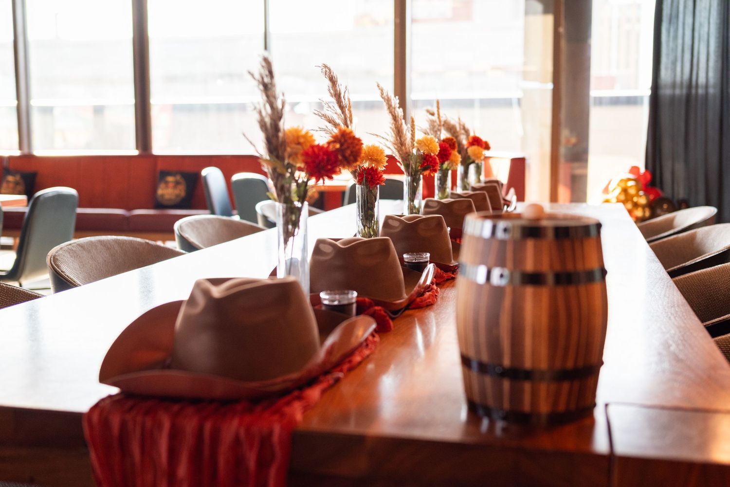 Elegant western-themed table setting with cowboy hats, wooden barrel, and orange floral centerpieces.