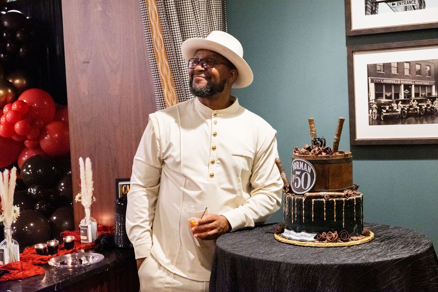 Man in white traditional outfit standing beside tiered 50th birthday cake at celebration party.