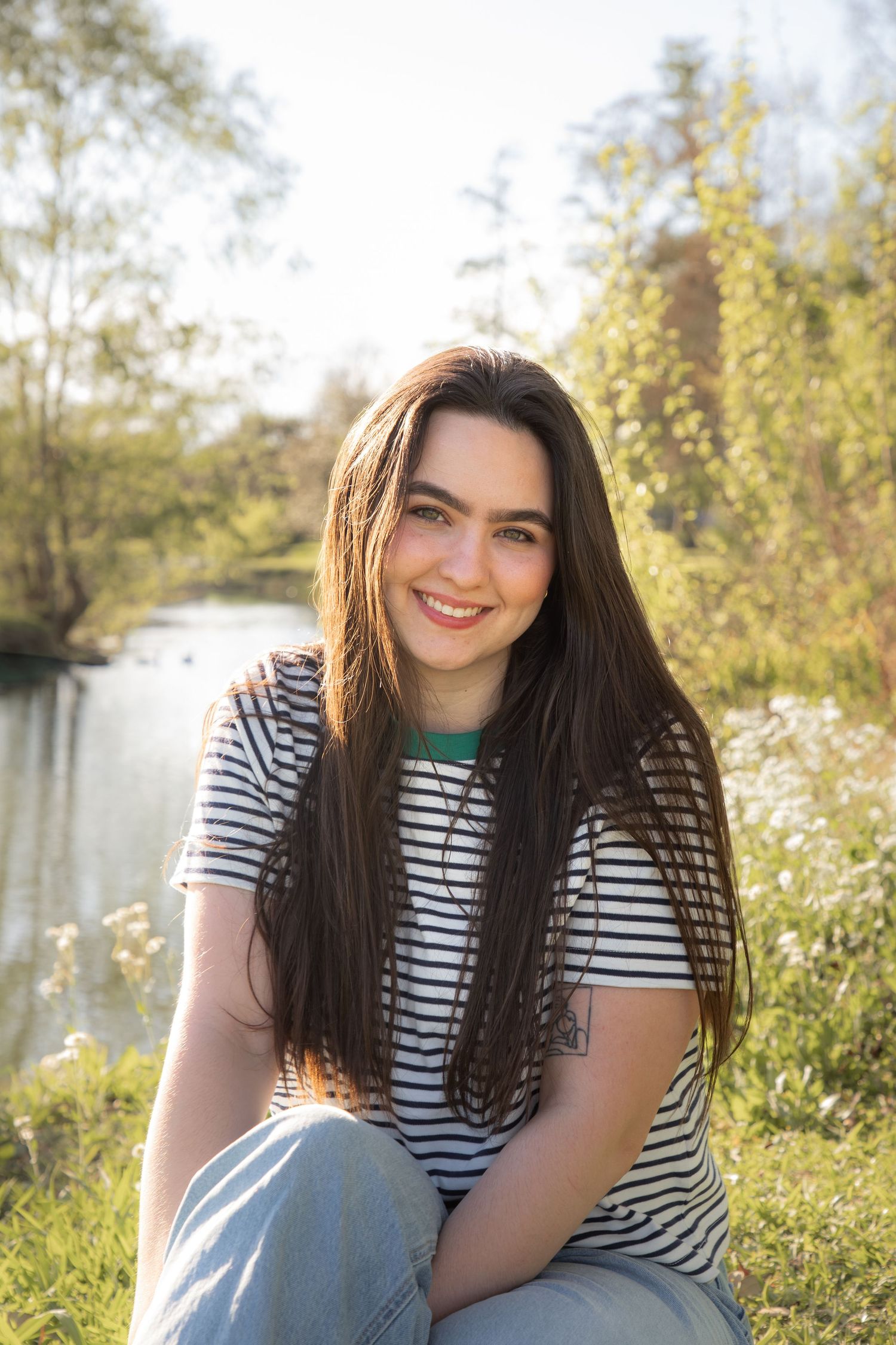Person in striped shirt sitting in sunny field with wildflowers.