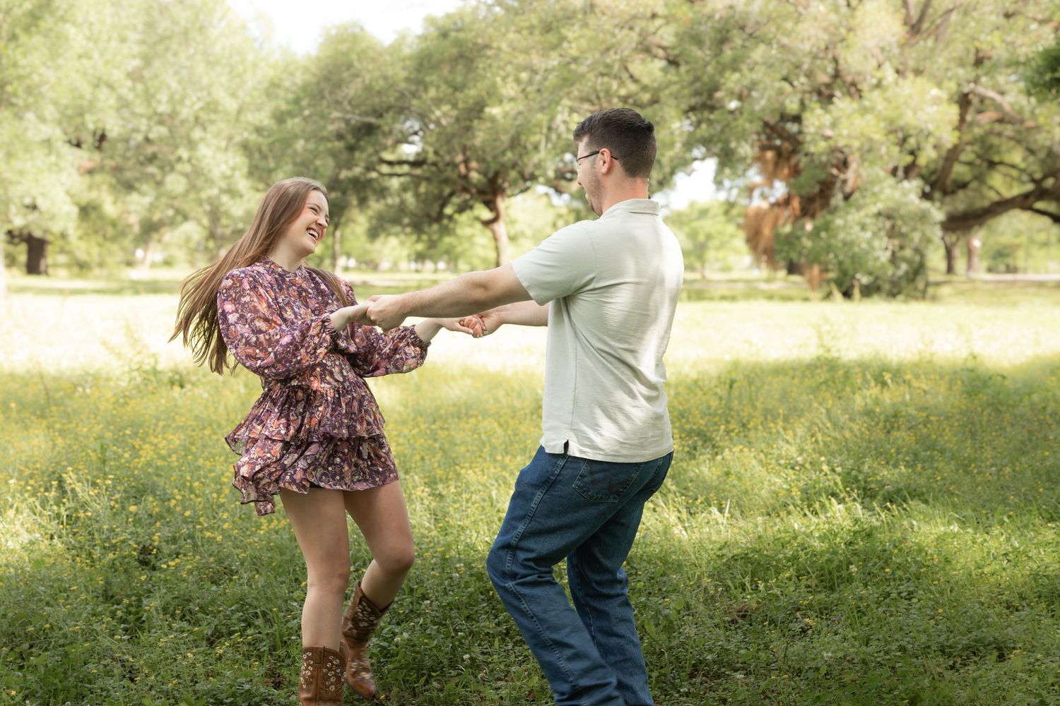 A couple dances joyfully in a lush green field, holding hands and spinning together outdoors.