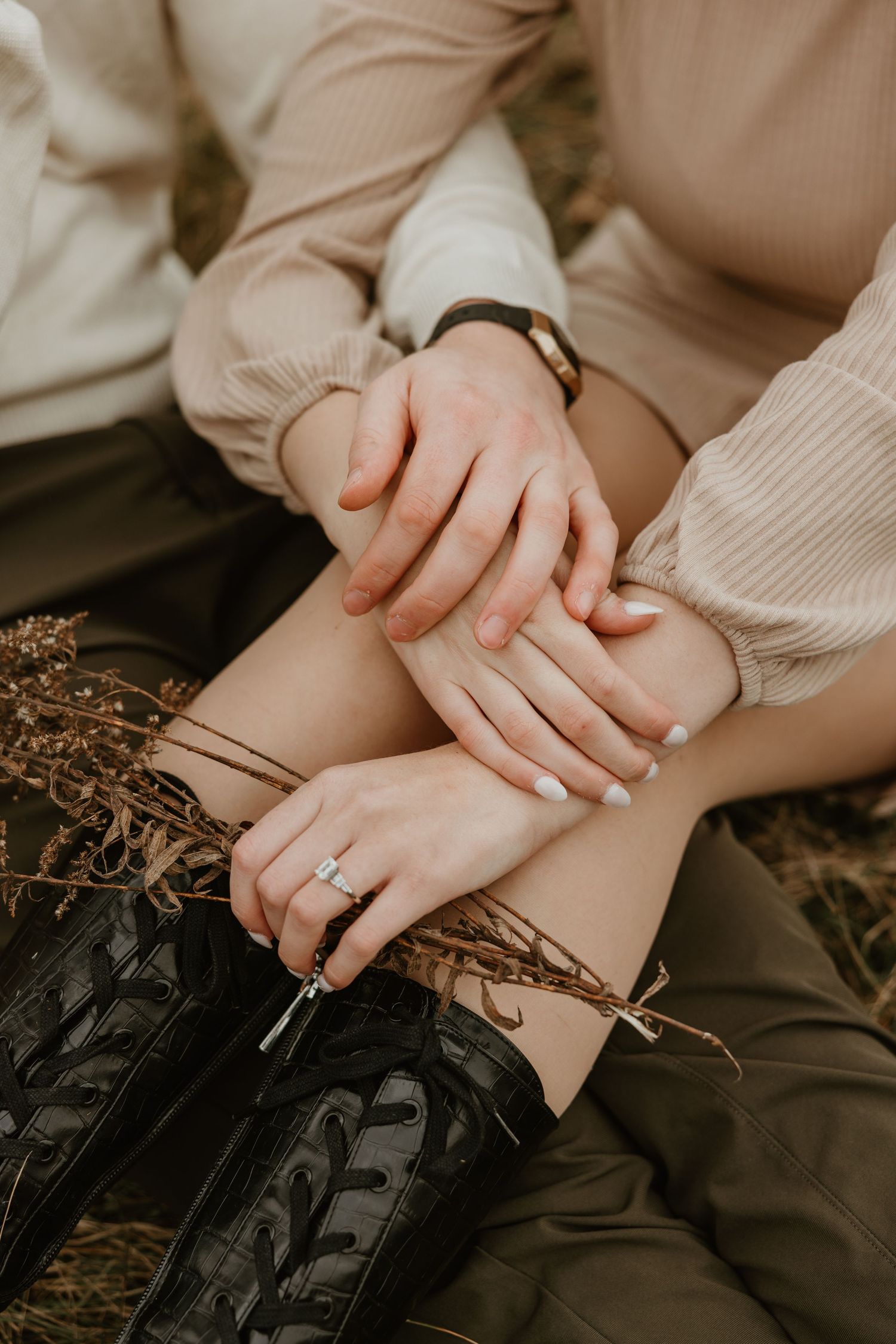 Close-up of a couple's hands with an engagement ring while sitting together in a field.