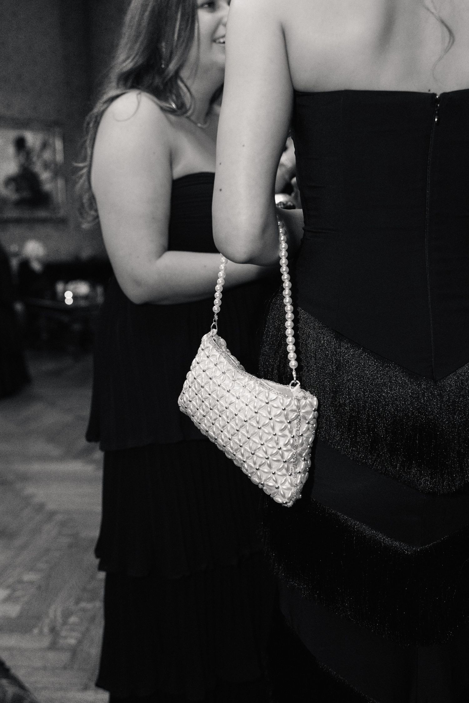 Woman in black strapless gown holding a white pearl clutch purse at a formal event.