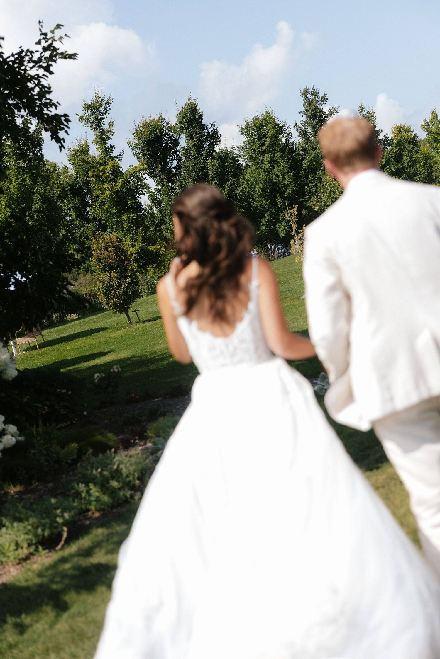 Bride and groom walking hand in hand through a green garden on their wedding day.