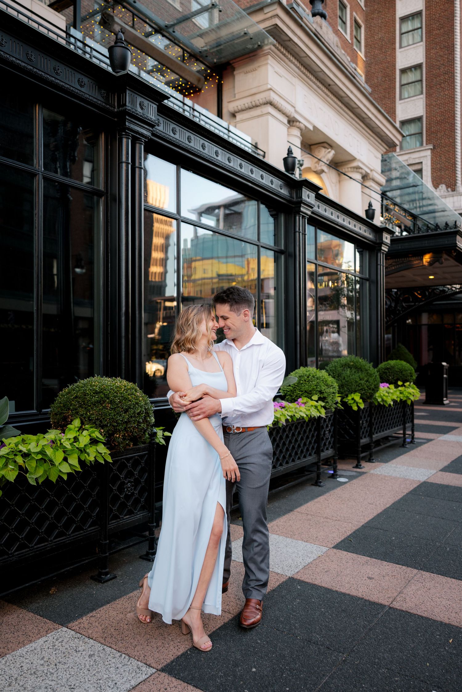 Couple embracing romantically outside an elegant urban restaurant with black facade and green topiaries.
