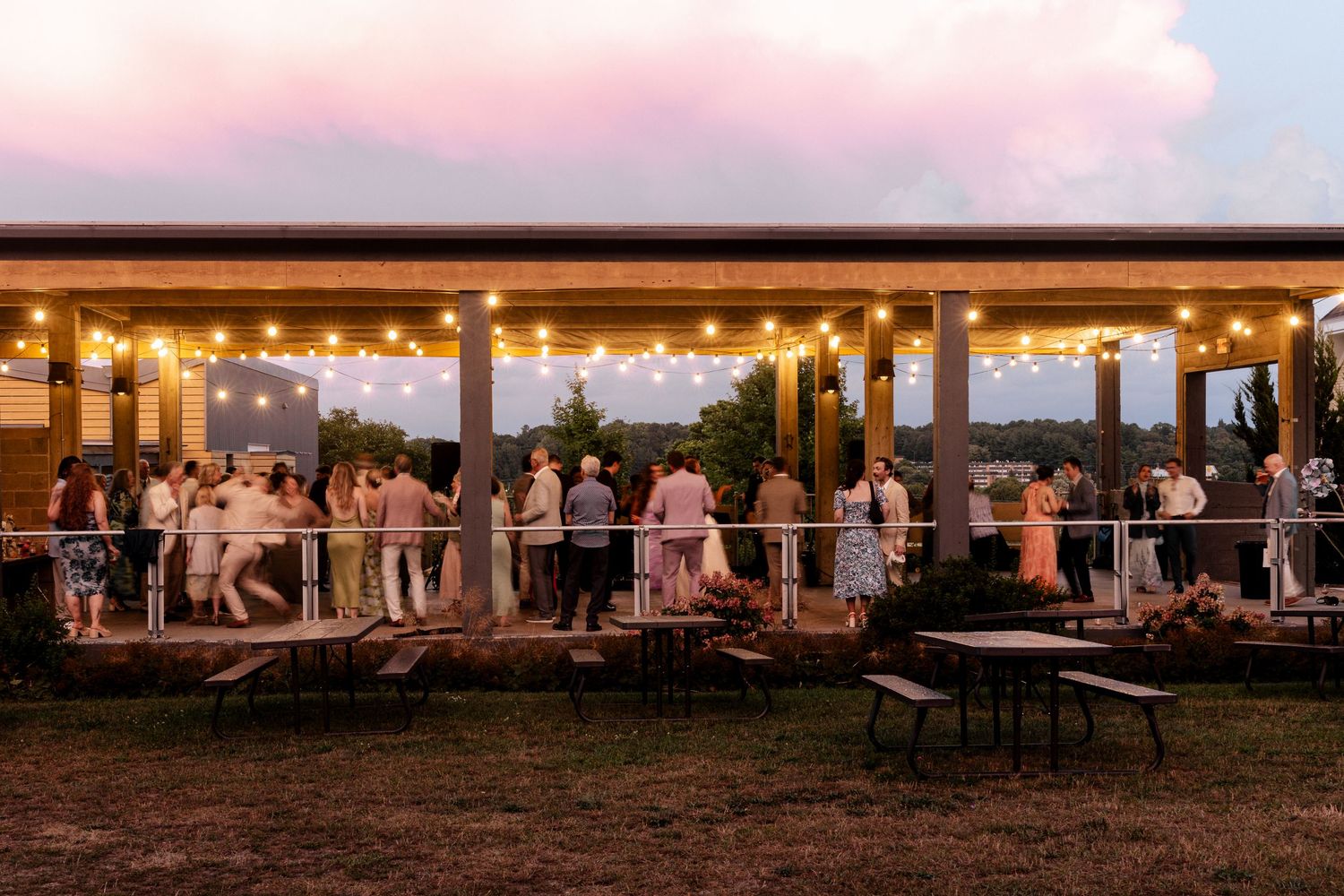 Outdoor evening wedding reception under string lights on a rustic patio at sunset with guests mingling.